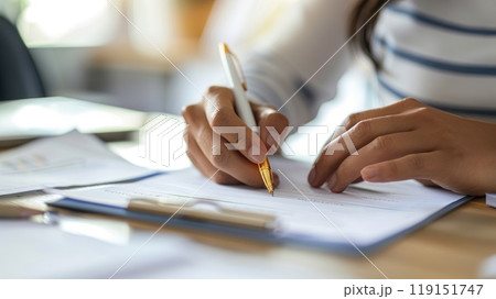 Hands of a business person holding a pen and reviewing documents at a office desk Hands of a business person holding a pen and reviewing documents at a office desk 119151747