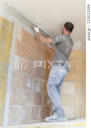 Craftsman in dirty gloves and gray shirt checking the ceiling surface with straight edge Craftsman in dirty gloves and gray shirt checking the ceiling surface with straight edge 119153364