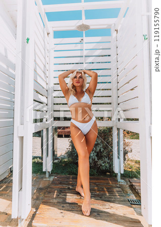 A woman in a bikini stands in front of a white shower stall. She is smiling and she is enjoying the moment 119155790