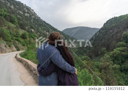 A couple is hugging each other on a mountain road. The man is wearing a blue shirt and the woman is wearing a black shirt. Scene is romantic and peaceful. 119155812