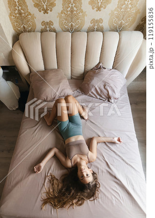 girl with long brown hair lays on a bed. She is smiling and her hair is flowing. 119155836