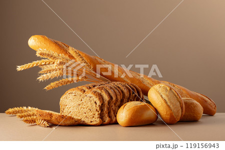 Sliced bread, baguette, and French buns with wheat ears on a beige background. 119156943