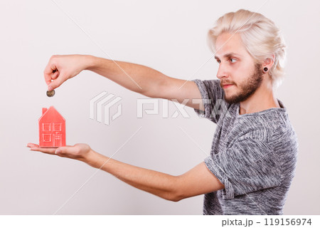Man putting coin into house piggybank 119156974