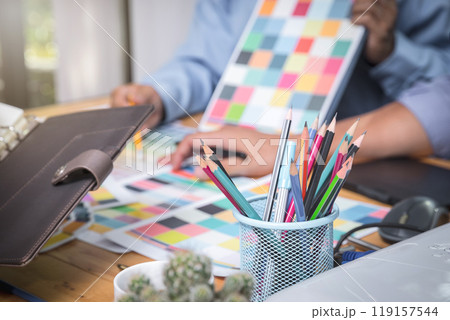 Several pencils in a pencil case over clothing designers working in background. 119157544