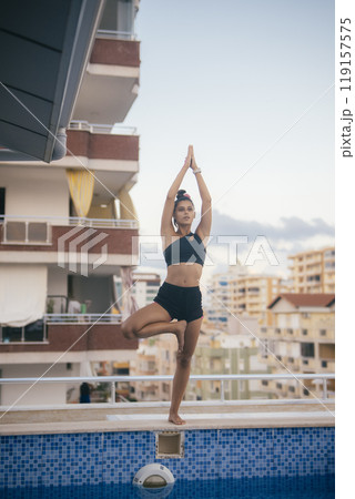 A Graceful Yoga Pose Performed Near a Pool with an Urban Backdrop in the Background 119157575