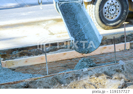 Concrete mixer pours fresh concrete on reinforced bars for new sidewalk Concrete mixer pours fresh concrete on reinforced bars for new sidewalk 119157727