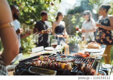Summer backyard barbecue party with friends gathered and food on barbecue grill 119159112