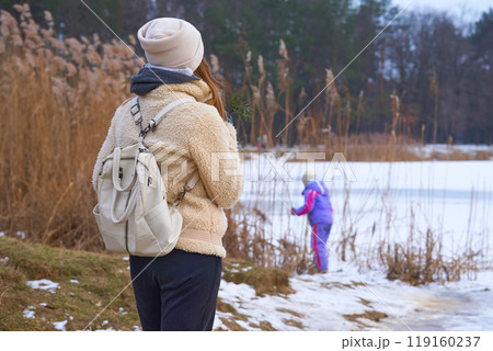 Mom and daughter walk on the shore of the winter frozen lake in the park 119160237