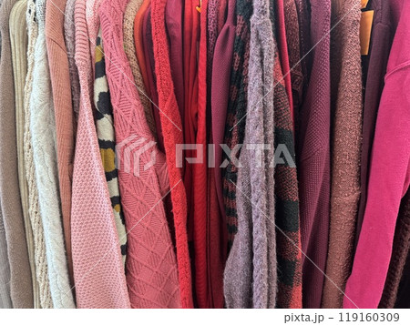various textured sweaters in shades of pink, red, and beige hanging on a rack various textured sweaters in shades of pink, red, and beige hanging on a rack 119160309