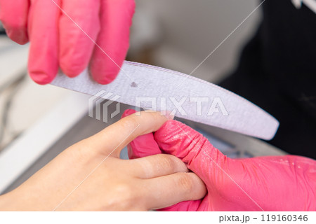 Skilled technician files nails carefully while providing a manicure to a client in a salon. 119160346