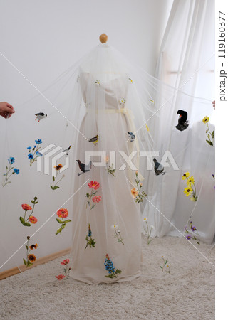 tulle fabric embroidery of flowers and birds on a veil On a thin fabric a woman embroiders straightening beautiful handwork on a mannequin wedding dress with bright decorations tulle fabric embroidery of flowers and birds on a veil On a thin fabric a woman embroiders straightening beautiful handwork on a mannequin wedding dress with bright decorations 119160377