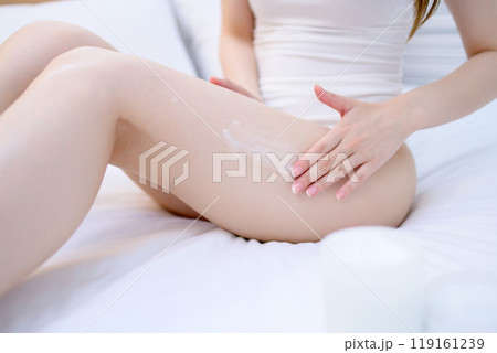 ベッドでボディクリームを脚に塗る下着姿の若いスレンダーな女性　スキンケア　ボディケア　フットケア 119161239