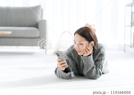 床に寝そべりスマホを見る女性 床に寝そべりスマホを見る女性 119166008