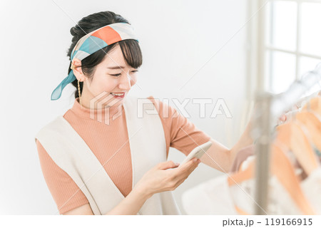スマホを持ちながら洋服の前に立つ女性（ファッション・アパレル・スタイリスト・ショップ店員） 119166915