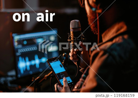 Studio streaming setup: a blogger livestreamer utilizing phone, podcast microphone for online streaming, reviewing business content, promoting through live broadcasts, enhancing digital presence. 119168159