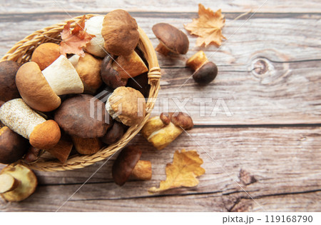 A woven basket filled with various mushrooms and autumn leaves on a wooden surface  119168790