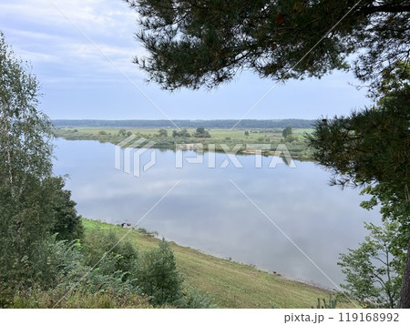 This tranquil photograph captures the serene beauty of a calm lake reflecting the surrounding lush green trees and clear blue sky. This tranquil photograph captures the serene beauty of a calm lake reflecting the surrounding lush green trees and clear blue sky. 119168992