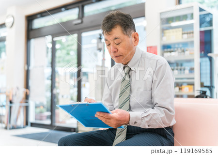 薬局の待合室で問診票に記入するシニア男性 119169585