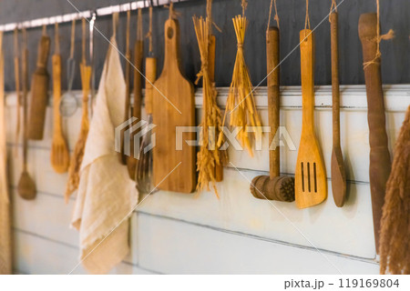 A rustic kitchen wall adorned with wooden utensils, dried herbs, and pasta in a cozy home setting 119169804