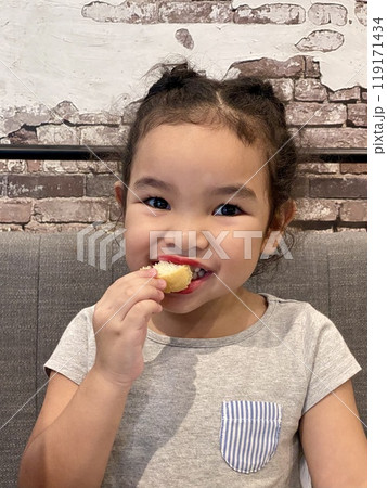 Portrait of a cute little girl eating shrimp cakes on the sofa in the living room 119171434
