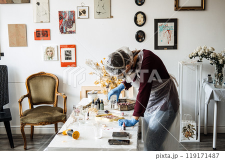 Artist preparing resin mixture in a home art studio, wearing protective gear. Essential tools and materials for setting up a functional creative workspace. 119171487