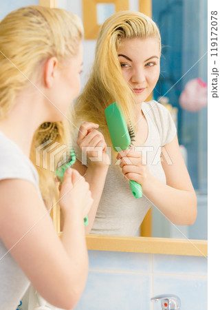 Woman brushing her blonde hair in bathroom Woman brushing her blonde hair in bathroom 119172078