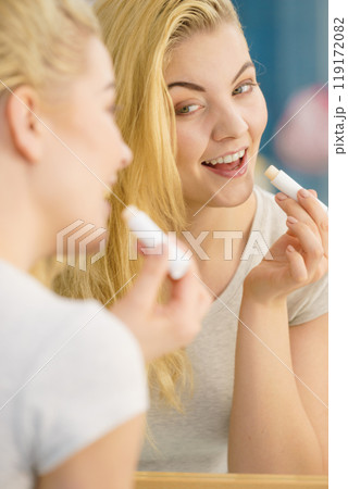 Woman in bathroom applying lip balm Woman in bathroom applying lip balm 119172082