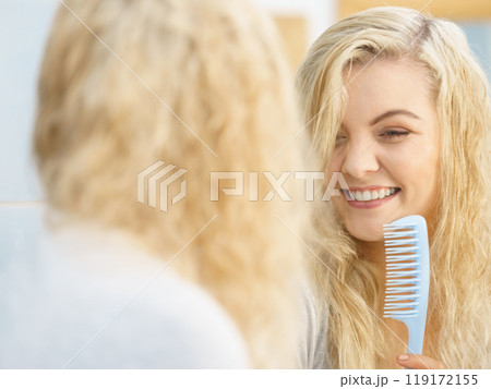 Woman getting ready in bathroom, combing hair. 119172155