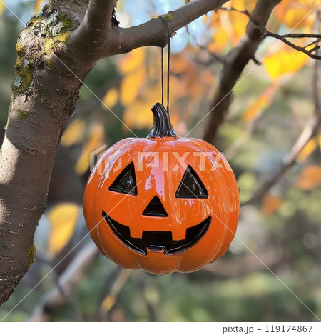 A spooky Halloween pumpkin is dangling from a tree branch above 119174867