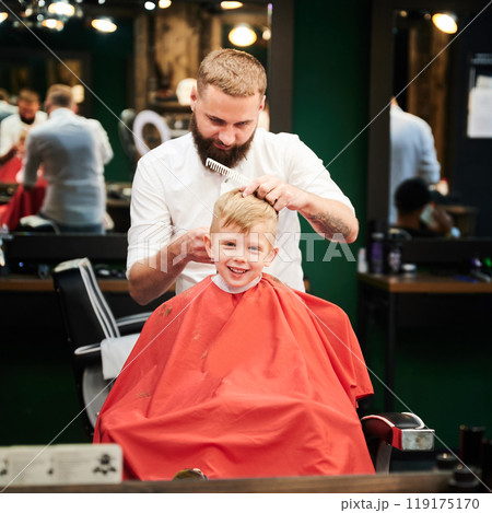 Barber using comb and shaver to cut hair. Professional hairdresser shaving little kid's nape. 119175170