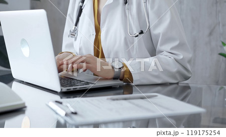 Doctor woman is using a laptop computer on a glass desk in medical office. Work place concept in Medicine Doctor woman is using a laptop computer on a glass desk in medical office. Work place concept in Medicine 119175254