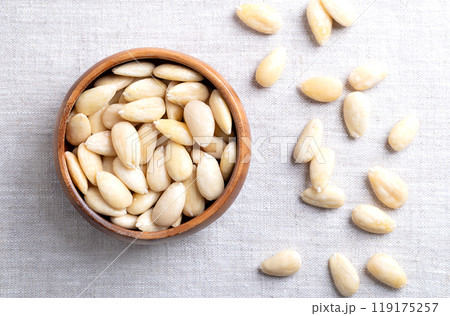 Freshly blanched almonds in a wooden bowl on linen. Shelled almonds that have been treated with hot water to soften the seed coat, which is then removed to reveal the seed. Fruits of Prunus amygdalus. 119175257