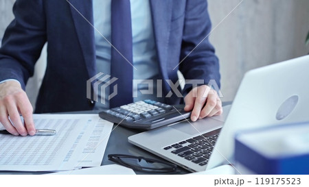 Businessman analyzing financial data on laptop and calculator. Close-up of a professional auditor working on financial reports. Business concept Businessman analyzing financial data on laptop and calculator. Close-up of a professional auditor working on financial reports. Business concept 119175523