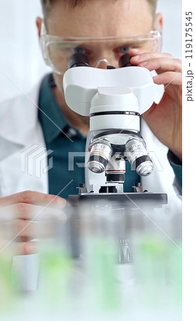 Man scientist with protective glasses using microscope in laboratory. Microbiology science concept Man scientist with protective glasses using microscope in laboratory. Microbiology science concept 119175545