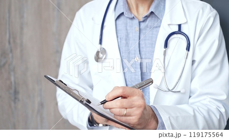 Healthcare professional doctor is focused on updating medical charts on a clipboard. Male unrecognizable physician at work. Medicine and pharmacy Healthcare professional doctor is focused on updating medical charts on a clipboard. Male unrecognizable physician at work. Medicine and pharmacy 119175564