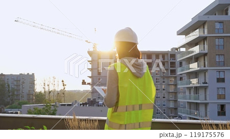 Construction female engineer taking notes and tapping on tablet computer while inspecting a building site at sunset. Industry development concept Construction female engineer taking notes and tapping on tablet computer while inspecting a building site at sunset. Industry development concept 119175576