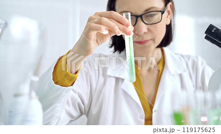 Scientist examining lab tube with a green fluid. Microbiology and science concept Scientist examining lab tube with a green fluid. Microbiology and science concept 119175625