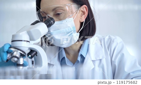 Female scientist in lab goggles, protective mask and gloves is using microscope in laboratory. Science concept Female scientist in lab goggles, protective mask and gloves is using microscope in laboratory. Science concept 119175682