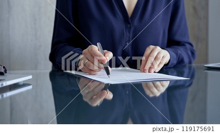 Businesswoman in dark blue blouse signing contract at the table. Close-up of a male executive signing a legal document on a glass desk. Business people concept 119175691