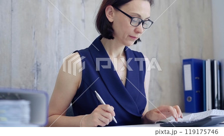 Businesswoman doing paperwork at her desk in the office, using calculator and taking notes. Taxes, audit in business Businesswoman doing paperwork at her desk in the office, using calculator and taking notes. Taxes, audit in business 119175746