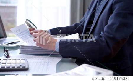 Businessman reviewing ring folder of financial documents with magnifying glass at desk in modern office. Audit and taxes in business 119175880
