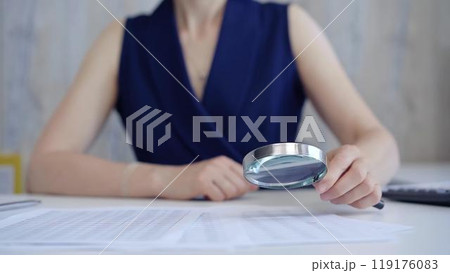 Businesswoman holding magnifying glass analyzing financial documents at office desk. Taxes, audit in business Businesswoman holding magnifying glass analyzing financial documents at office desk. Taxes, audit in business 119176083