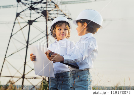 Little kids pretending engineers or managers with safety helmets, reading papers documents. Electrical industry profession, serious smart children on transmission power lines background. 119178075