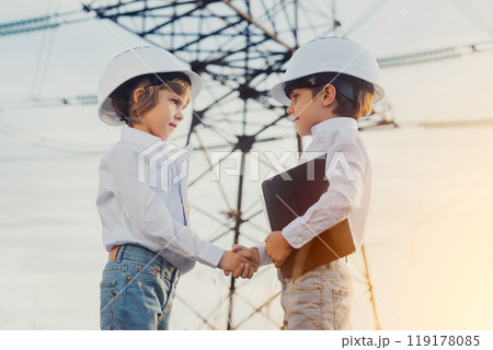 Little kids shaking hands. Handshake, welcome to team, introduction or hiring. Electrical industry job, serious smart children on Electricity Pylons background. Green energy sustainability, renewable 119178085