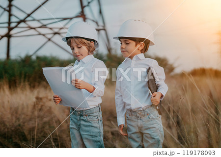 Little kids playing as engineers or managers with safety helmets, using tablet. Electrical industry profession, serious smart children on transmission power lines background. Little kids playing as engineers or managers with safety helmets, using tablet. Electrical industry profession, serious smart children on transmission power lines background. 119178093