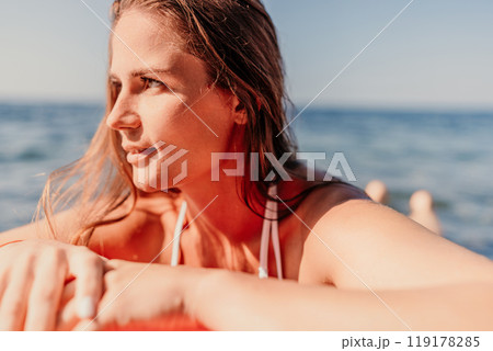 A woman with long hair is laying on a red surfboard in the ocean A woman with long hair is laying on a red surfboard in the ocean 119178285