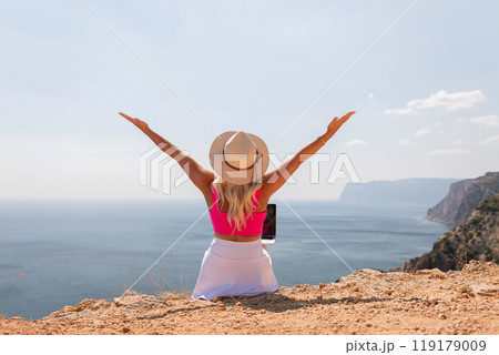 A woman is sitting on a beach with her arms outstretched, wearing a pink top 119179009