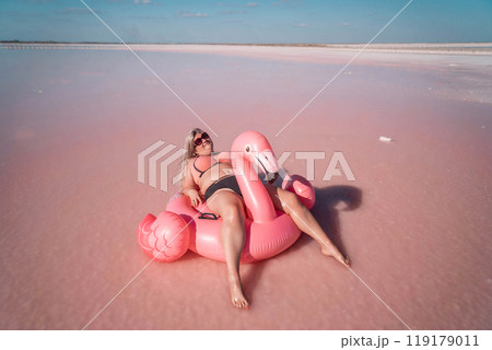 Pink Lake Flamingo Float Summer Vacation - Woman enjoys summer vacation on a pink inflatable flamingo float in a pink lake. Pink Lake Flamingo Float Summer Vacation - Woman enjoys summer vacation on a pink inflatable flamingo float in a pink lake. 119179011