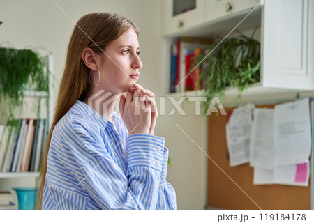 Serious young woman looking out the window, in home interior 119184178
