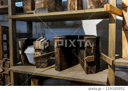 Set of wooden molds with a white ceramic vase placed on a shelf in a glassblowing factory. The rustic setting highlights traditional craftsmanship and manual production methods 119185052
